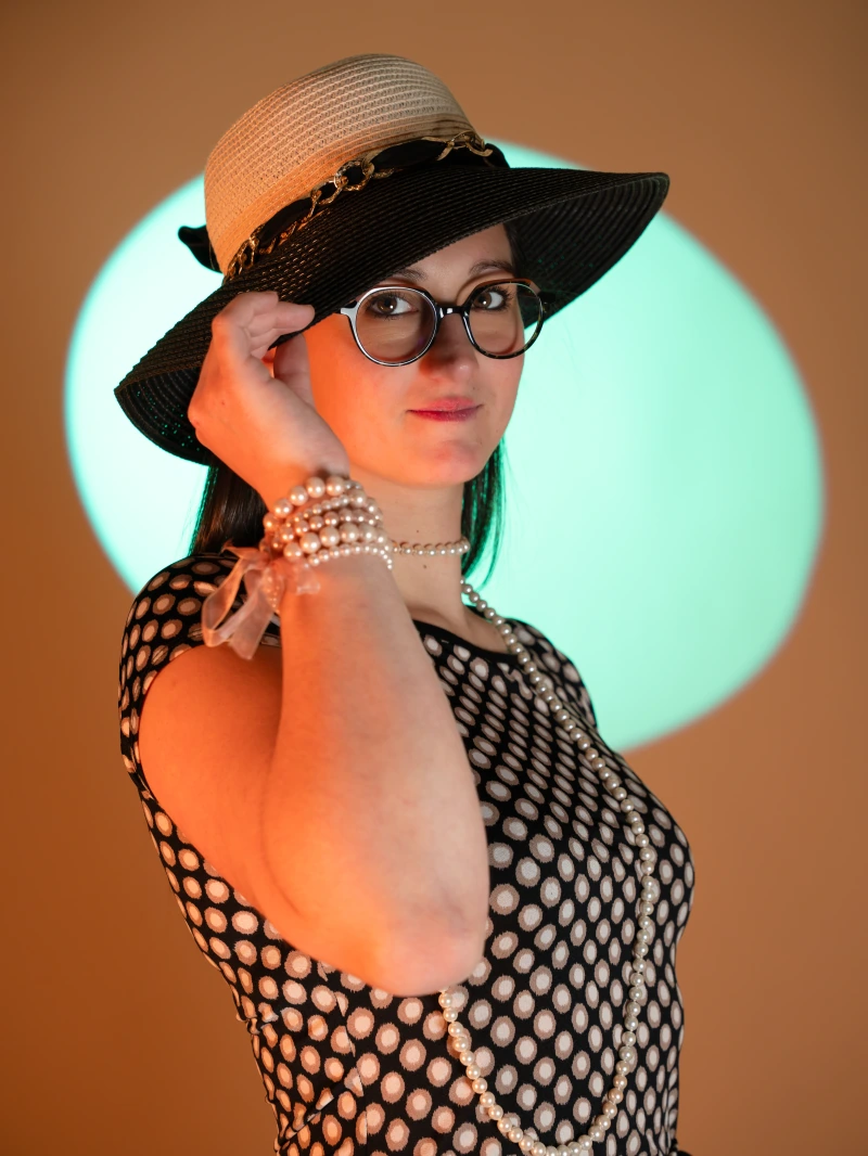 Portrait en studio avec chapeau, perles et lumière colorée
